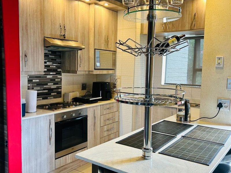 Modern kitchen featuring light wood-grain cabinetry, stone countertops, a gas hob, built-in oven, and a functional breakfast bar with integrated storage.