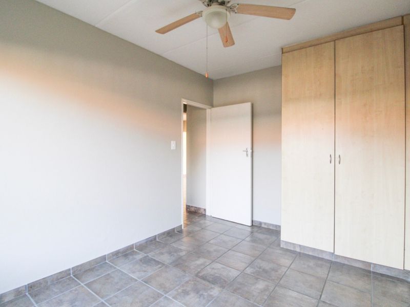 A clean, empty bedroom featuring neutral walls, tiled flooring, a ceiling fan, and built-in wooden cupboards.