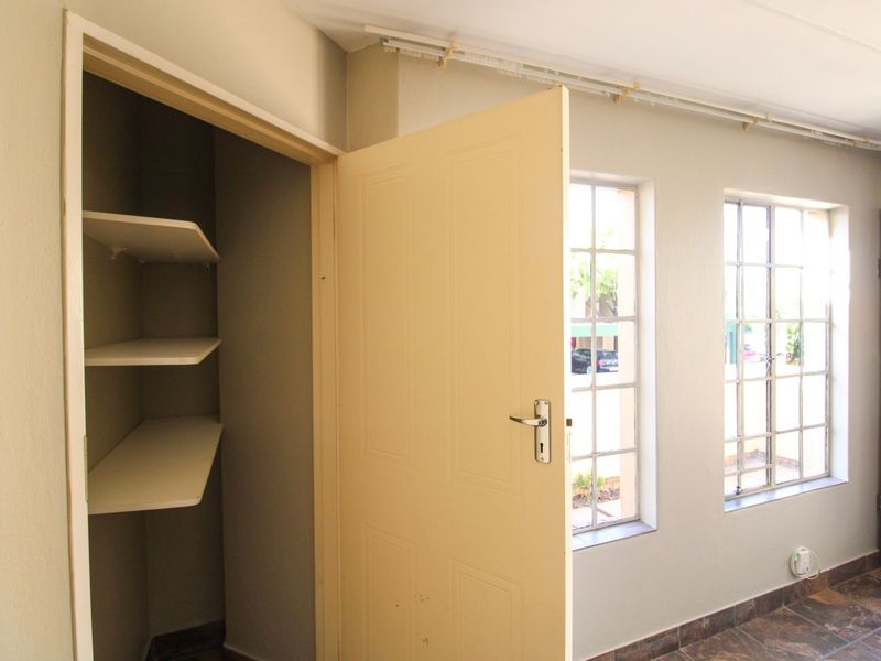 An empty bedroom featuring tiled flooring, built-in shelving, and metal-framed windows, offering a clean and functional space ready for personalization.