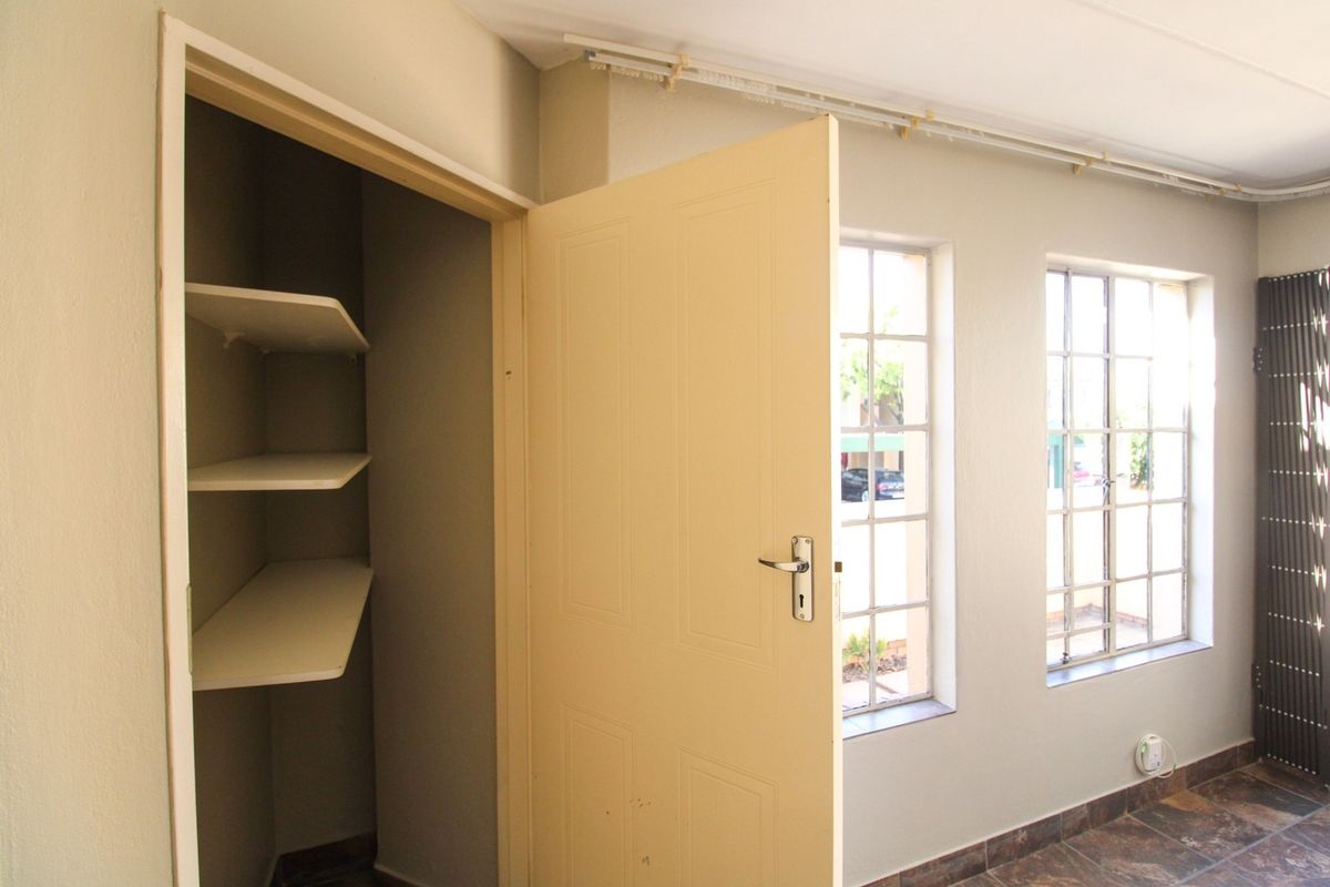 An empty bedroom featuring tiled flooring, built-in shelving, and metal-framed windows, offering a clean and functional space ready for personalization.