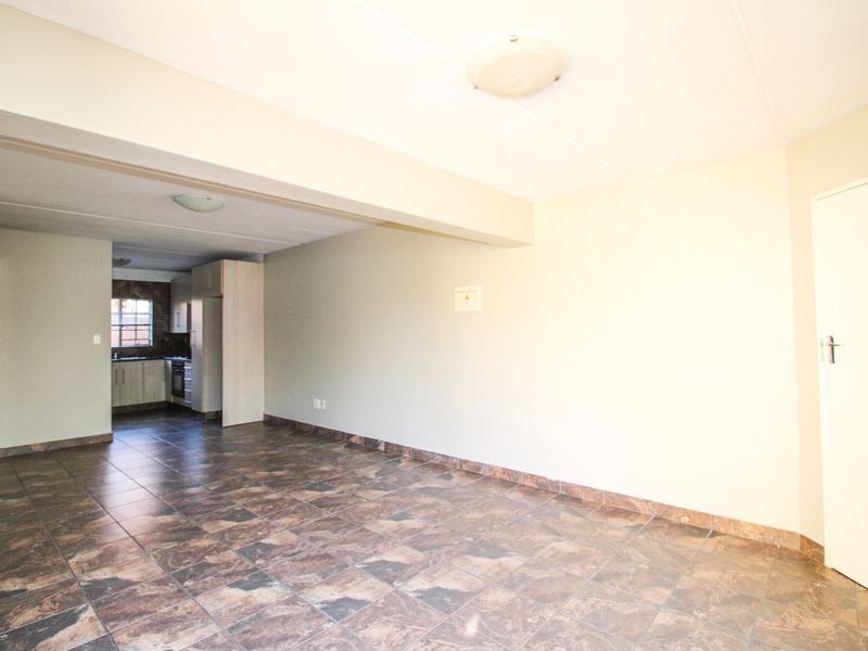 An open-plan living area featuring tiled flooring and a connected kitchen space with built-in cabinetry and appliances.