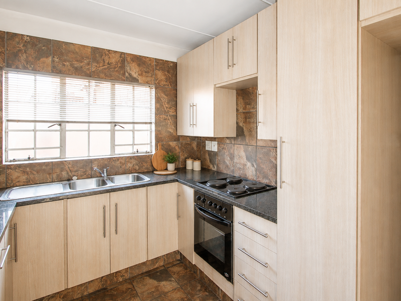 A functional kitchen featuring light wood-finish cabinetry, dark laminate countertops, a built-in oven and hob, and a tiled backsplash with a double sink.