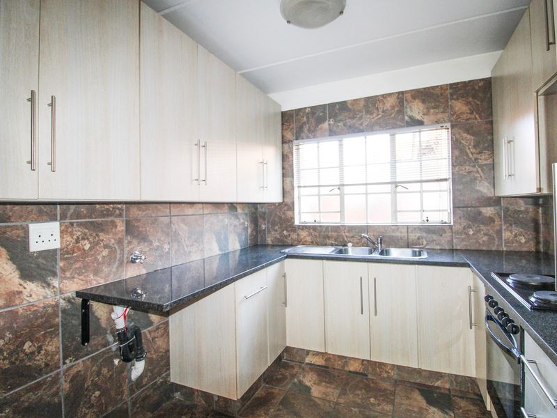 A functional kitchen featuring light wood-finish cabinetry, dark granite countertops, tiled walls and flooring, and a built-in oven with electric hob.