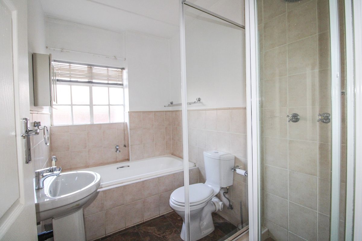 A functional bathroom featuring a pedestal basin, built-in bathtub, and a separate glass-enclosed shower with neutral wall tiling.