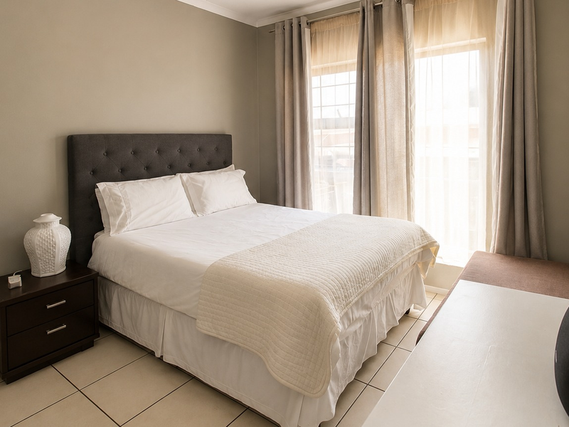 A well-lit bedroom featuring neutral wall tones, tiled flooring, and a sliding glass door providing access to the exterior.
