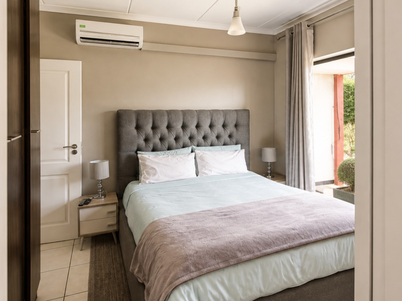 A well-maintained bedroom featuring tiled flooring, a built-in wardrobe, and a split-system air conditioner, with direct access to an outdoor patio area.