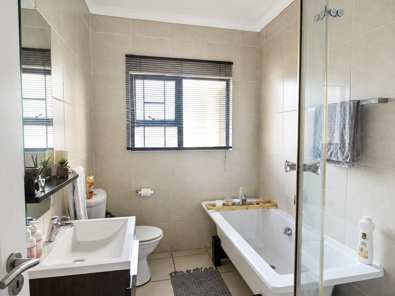 A well-maintained bathroom featuring a vanity basin, a bathtub, and a separate shower enclosure with neutral wall and floor tiling.