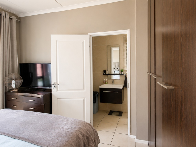 A well-maintained bedroom featuring built-in cupboards, tiled flooring, and direct access to an en-suite bathroom with a modern vanity.