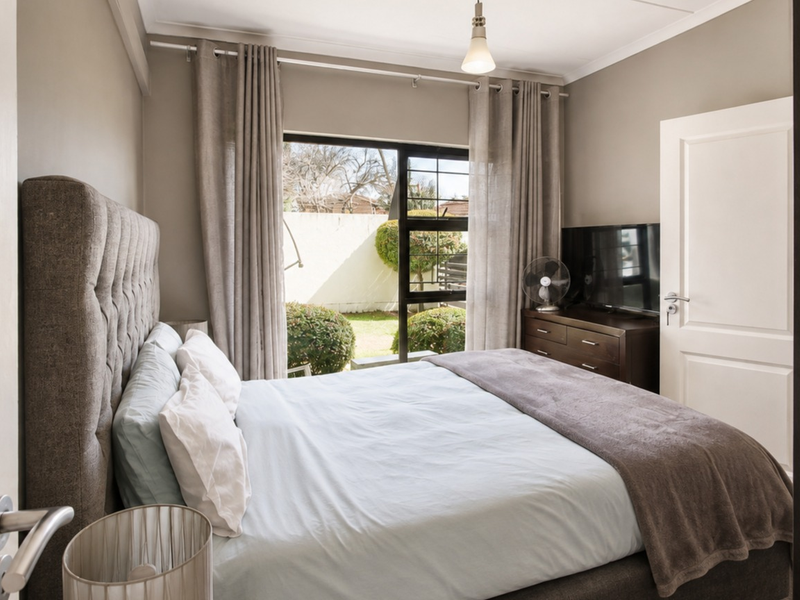 A well-maintained bedroom featuring neutral wall tones, a sliding door providing access to the garden, and classic coving detail.