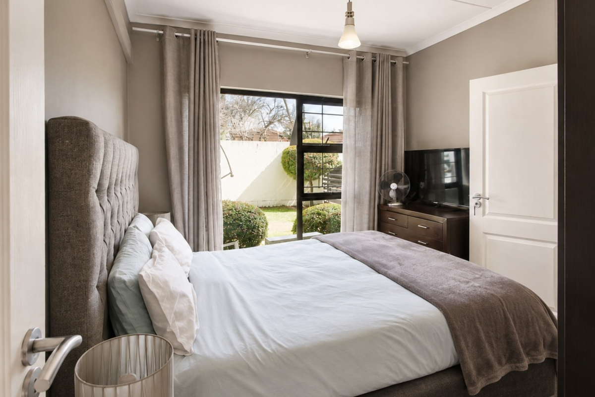 A well-maintained bedroom featuring neutral wall tones, a sliding door providing access to the garden, and classic coving detail.