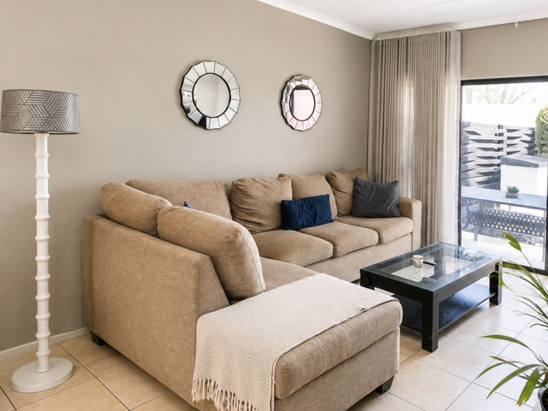 A comfortable living room featuring neutral wall tones, tiled flooring, and a large sliding glass door providing access to the outdoor patio area.