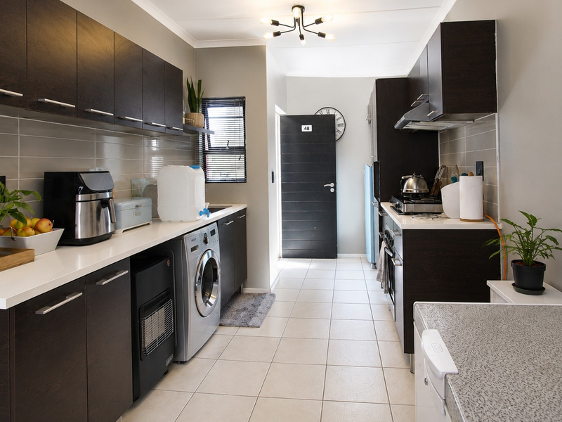 Modern kitchen featuring dark wood cabinetry, white stone countertops, tiled backsplash, and integrated laundry facilities with a gas hob and built-in oven.