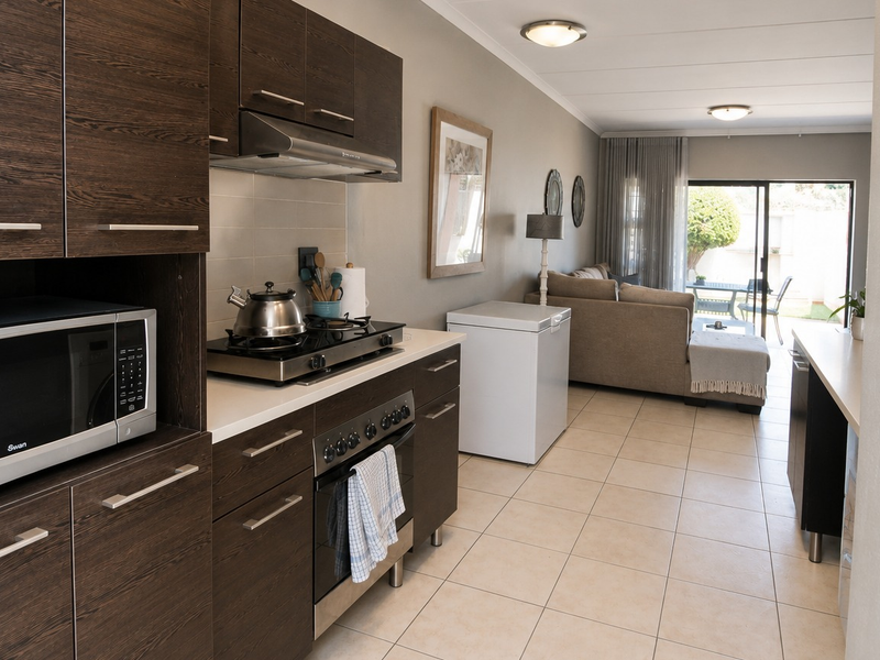 Open-plan kitchen and living area featuring dark wood cabinetry, gas hob, tiled flooring, and direct access to an outdoor patio through sliding glass doors.