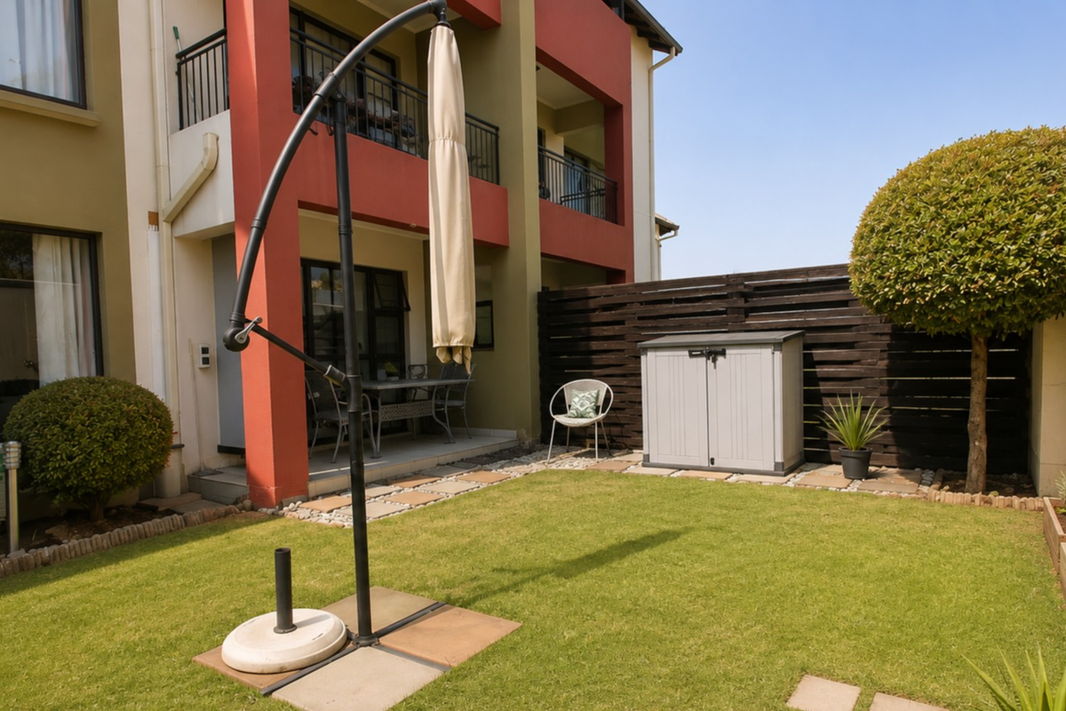 A well-maintained rear garden featuring a manicured lawn, timber privacy fencing, raised garden beds, and access to a covered patio area.