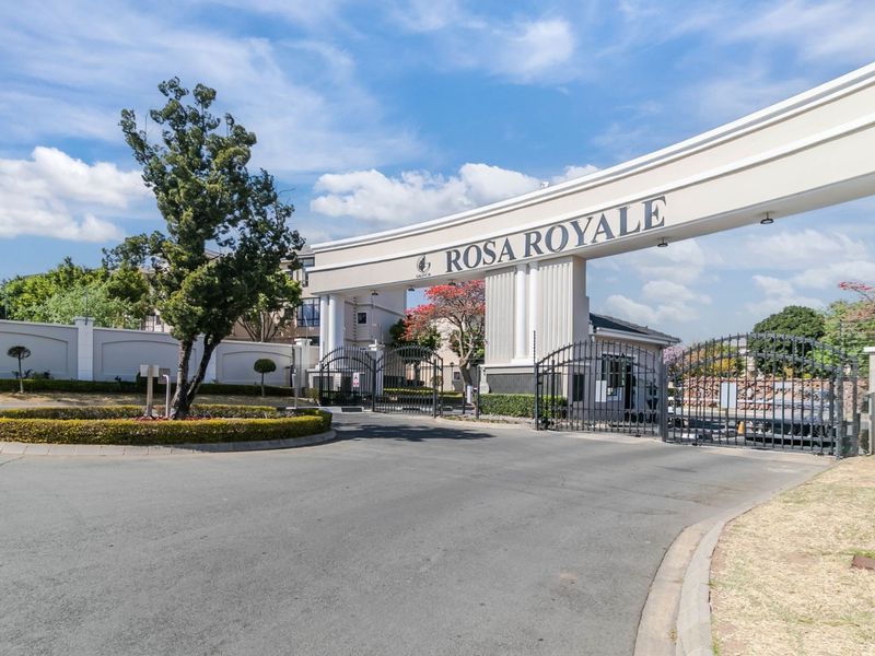 The main entrance gate and security access point for the Rosa Royale apartment complex, featuring a prominent archway and perimeter security fencing.
