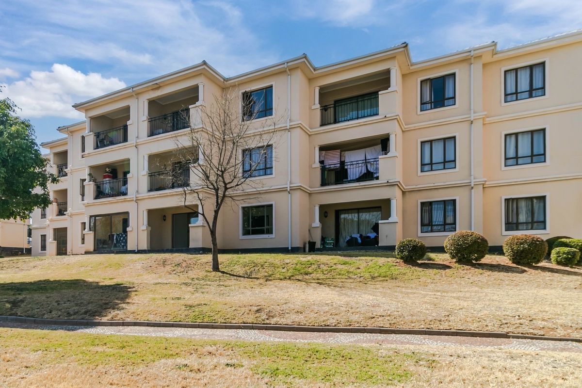Rear elevation of a multi-story apartment complex featuring private balconies with metal railings and sliding glass doors overlooking a landscaped lawn area.