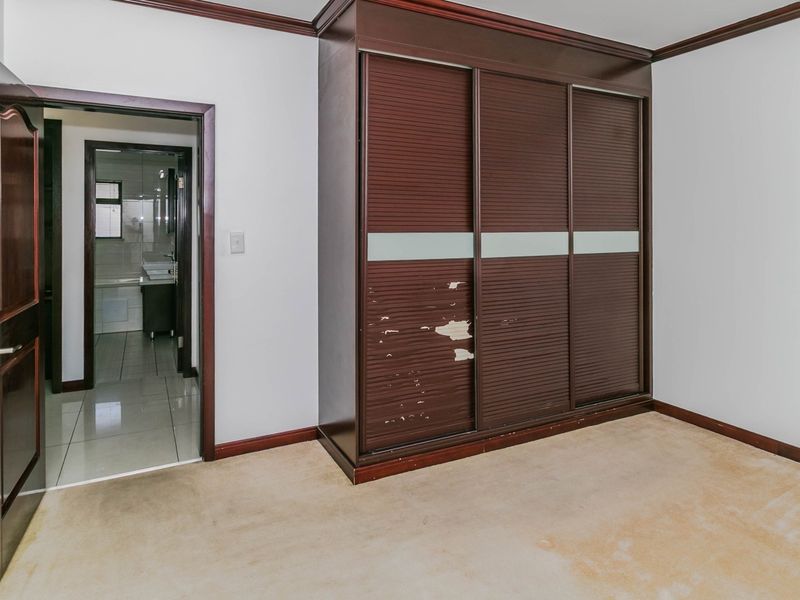 A bedroom featuring built-in wardrobes with visible wear and carpeted flooring, with an adjacent en-suite bathroom visible through the doorway.