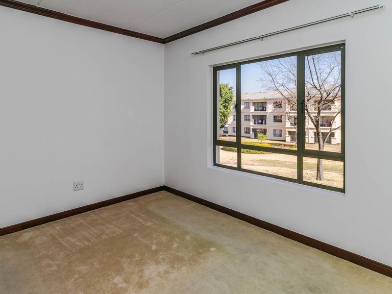 An empty bedroom featuring neutral walls, dark timber-look skirting boards, and a large window with views of the surrounding apartment complex.