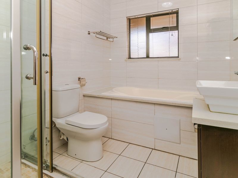 A clean, functional bathroom featuring a built-in bathtub, separate shower enclosure, toilet, and a vanity basin with tiled finishes throughout.