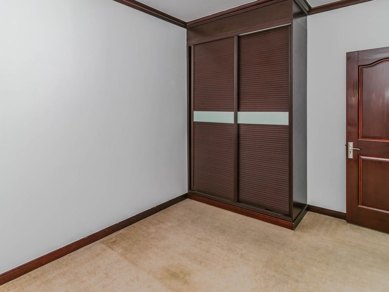 An empty bedroom featuring a built-in dark wood wardrobe, carpeted flooring, and a solid timber door.
