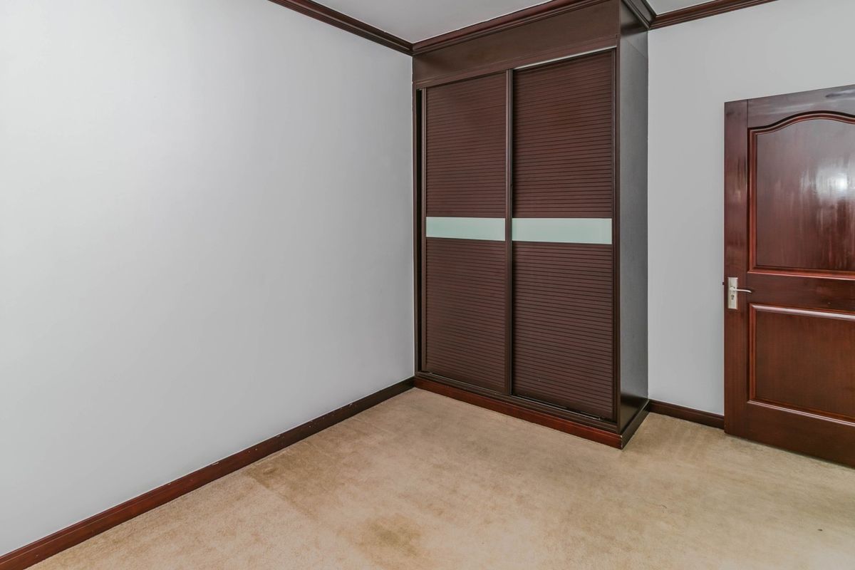 An empty bedroom featuring a built-in dark wood wardrobe, carpeted flooring, and a solid timber door.