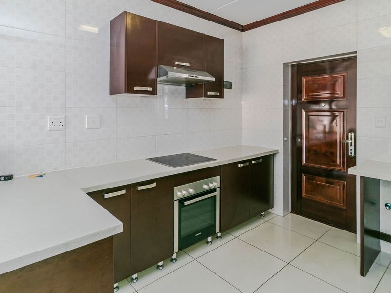 A clean, modern kitchen featuring dark wood cabinetry, stone countertops, integrated oven and hob, and tiled finishes throughout.