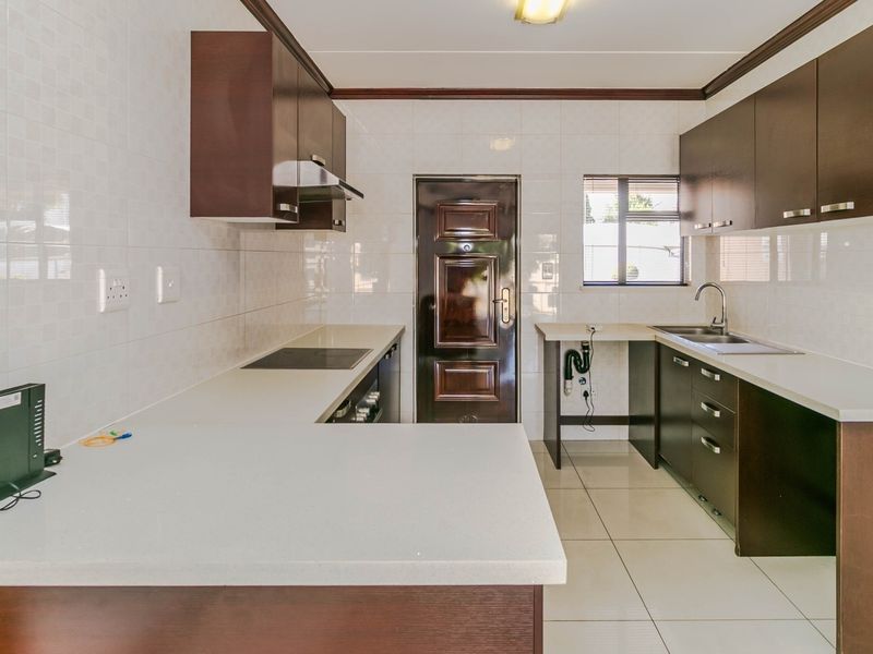 A functional kitchen featuring dark wood cabinetry, light countertops, tiled backsplash, and an electric hob, with an adjacent exterior door.