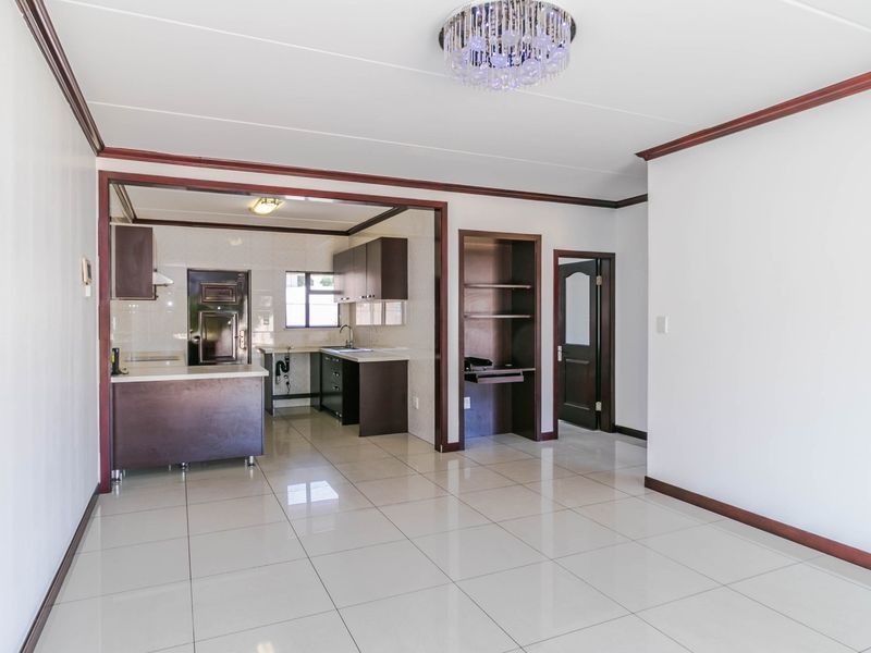 Spacious open-plan living and kitchen area featuring tiled flooring, built-in cabinetry, and crown molding, offering a clean and versatile layout.