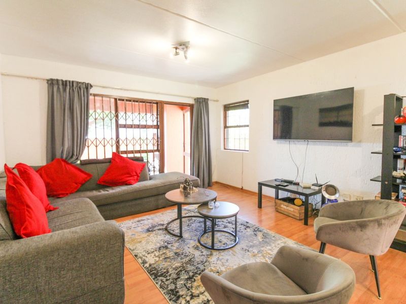 A comfortable living room featuring laminate flooring, a sliding glass door with security gate, and wall-mounted television space.