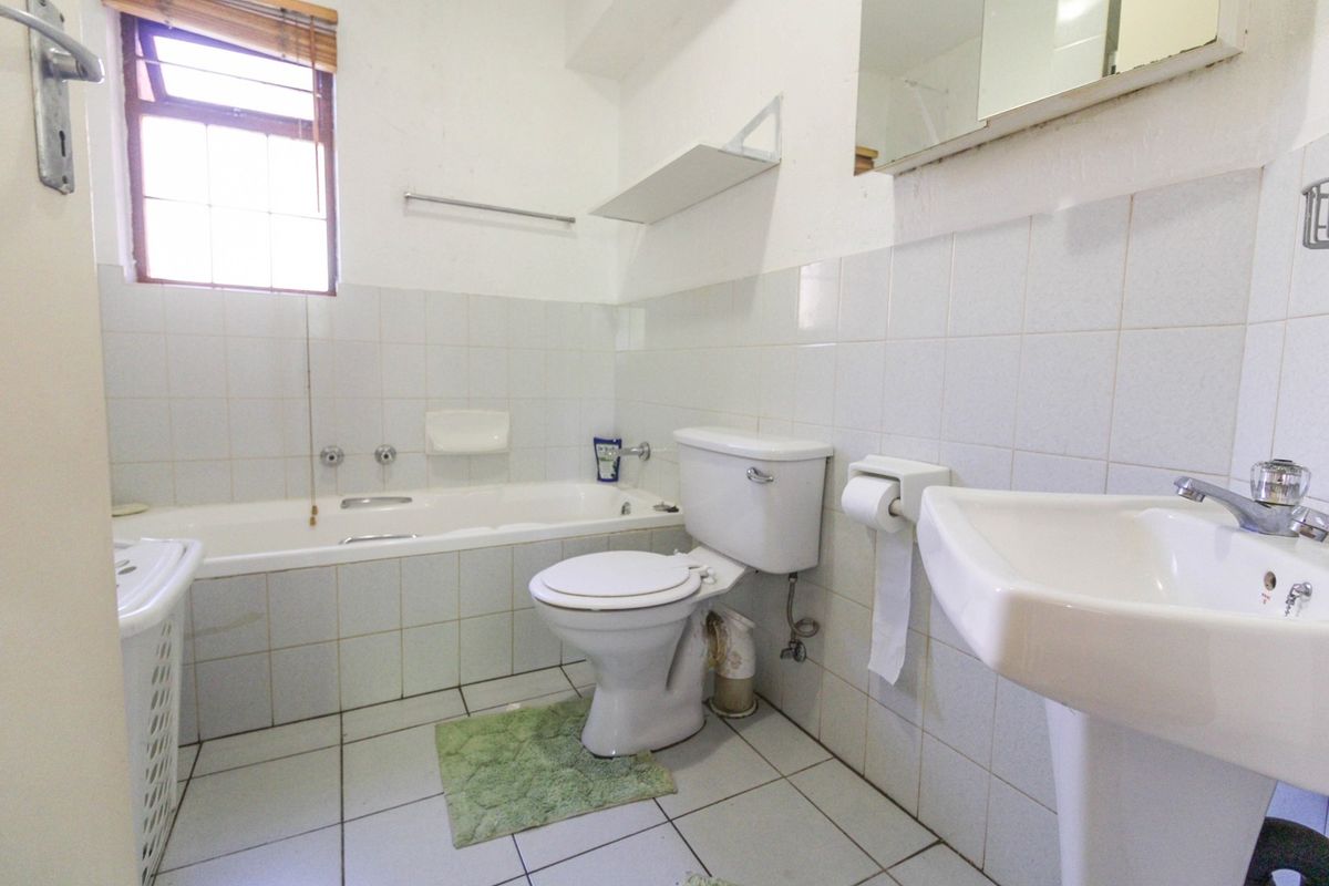 A functional bathroom featuring a bathtub, pedestal basin, and toilet with white tiled finishes, offering potential for modernization and cosmetic updates.