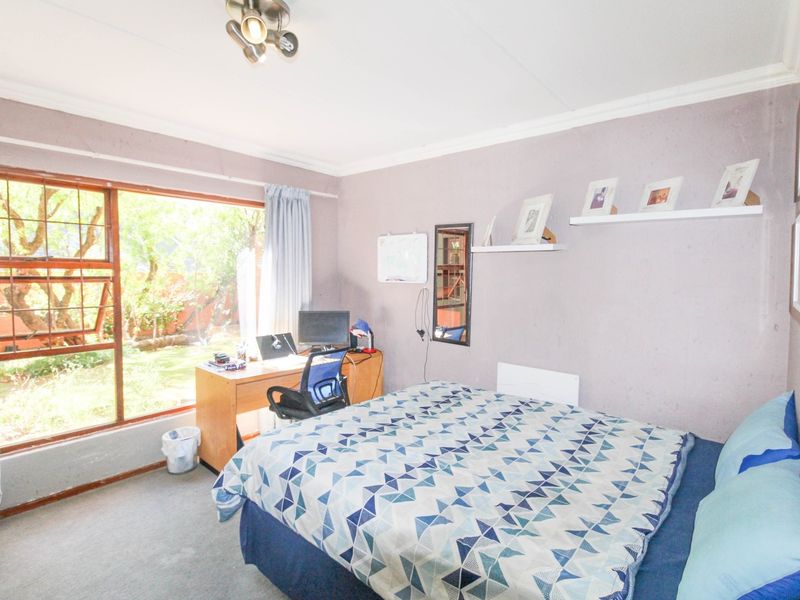 A bedroom featuring a large window with garden views, neutral wall finishes, and built-in shelving.