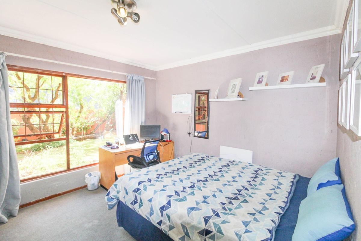 A bedroom featuring a large window with garden views, neutral wall finishes, and built-in shelving.