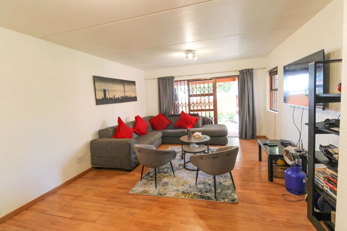 A comfortable living room featuring laminate flooring and a sliding door that provides access to the outdoor area through a security gate.