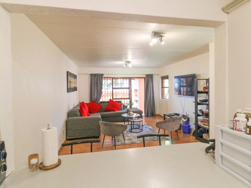 Open plan living area featuring laminate flooring, ceiling spotlights, and a sliding door leading to an outdoor space with security gate.