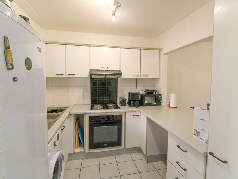 Compact kitchen featuring white cabinetry, built-in oven with electric hob, extractor fan, tiled backsplash, and tiled flooring.