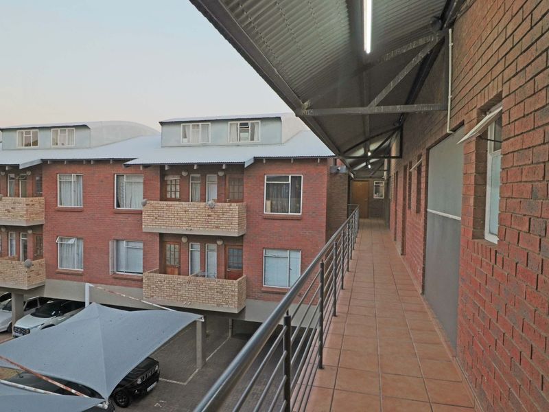 An exterior elevated walkway featuring tiled flooring, a metal balustrade, and a corrugated roof, providing access to apartment units.