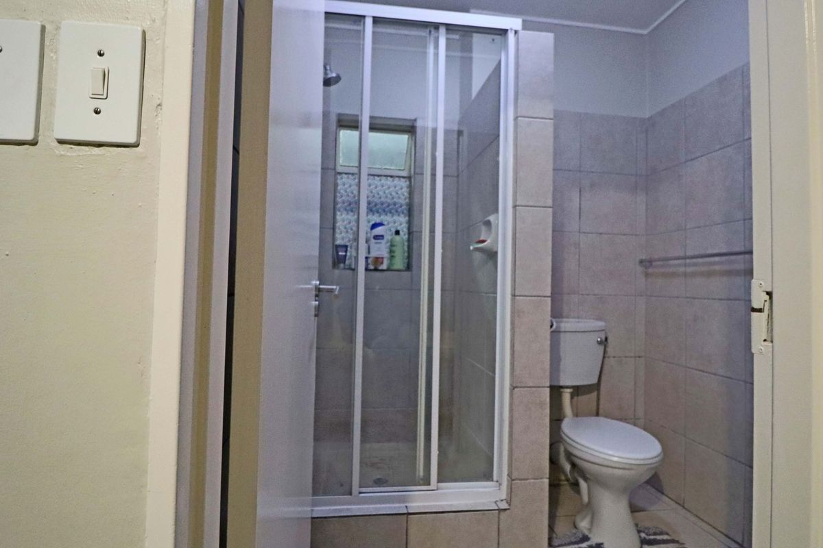 A functional bathroom featuring a shower enclosure, toilet, and neutral wall tiling. The space is well-maintained but offers potential for modern updates.