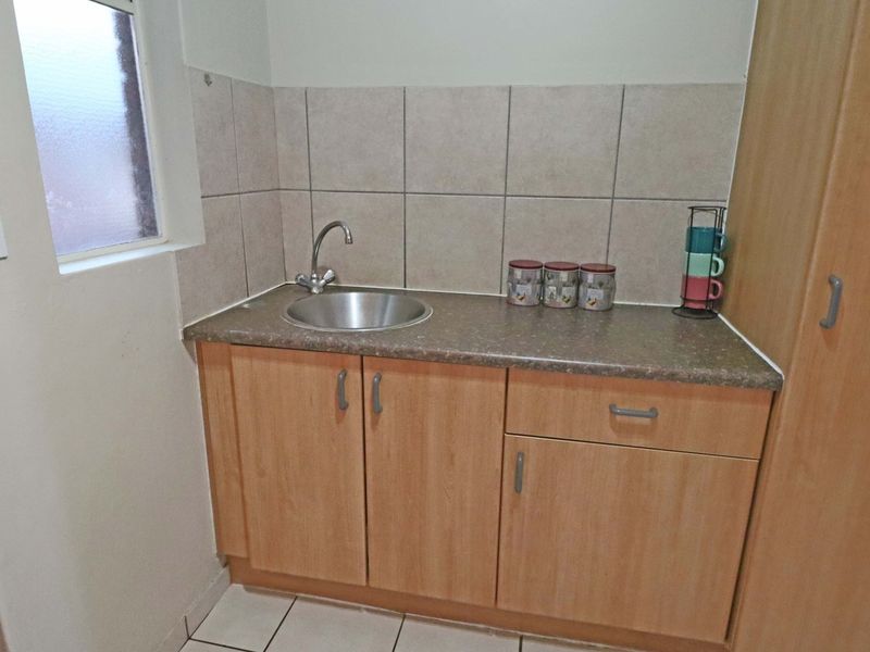 A compact scullery area featuring built-in wooden cabinetry, a stainless steel sink, tiled splashback, and tiled flooring.
