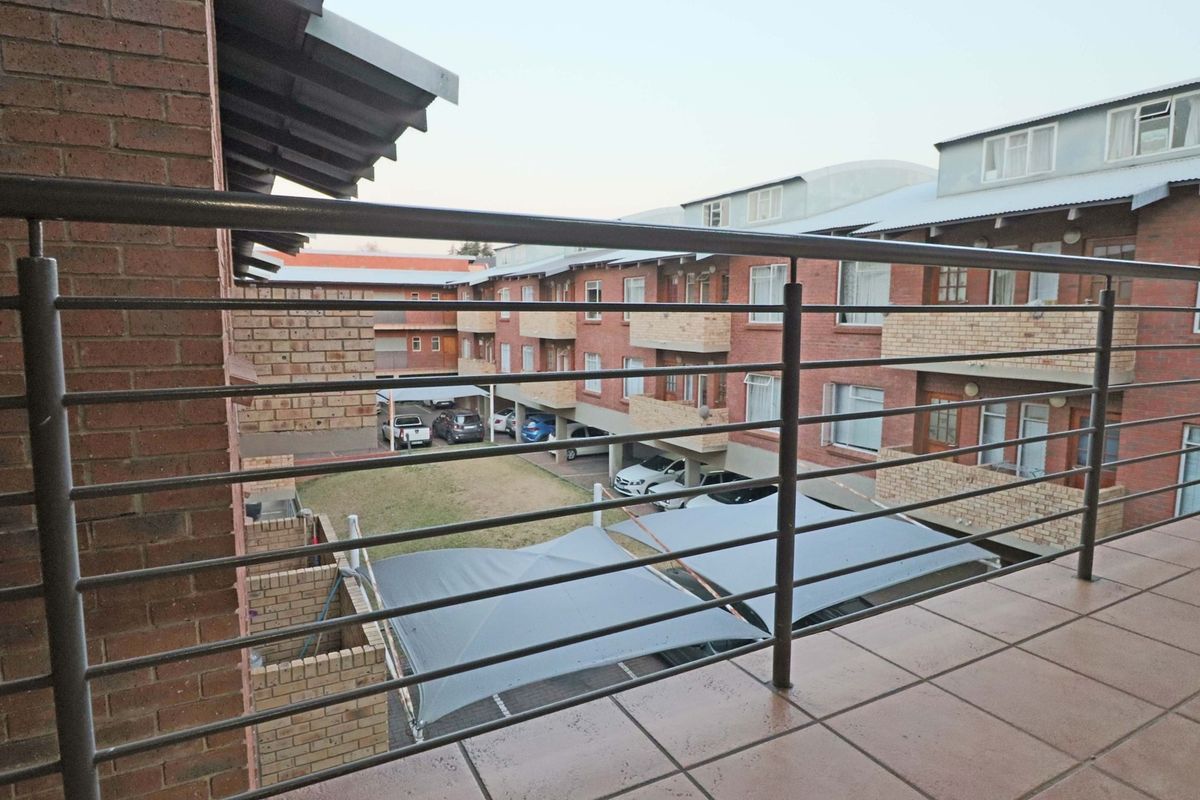 A view from a tiled balcony overlooking the apartment complex courtyard, featuring a metal balustrade and covered parking bays below.