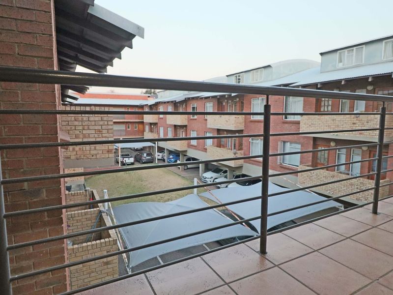 A view from a tiled balcony overlooking the apartment complex courtyard, featuring a metal balustrade and covered parking bays below.