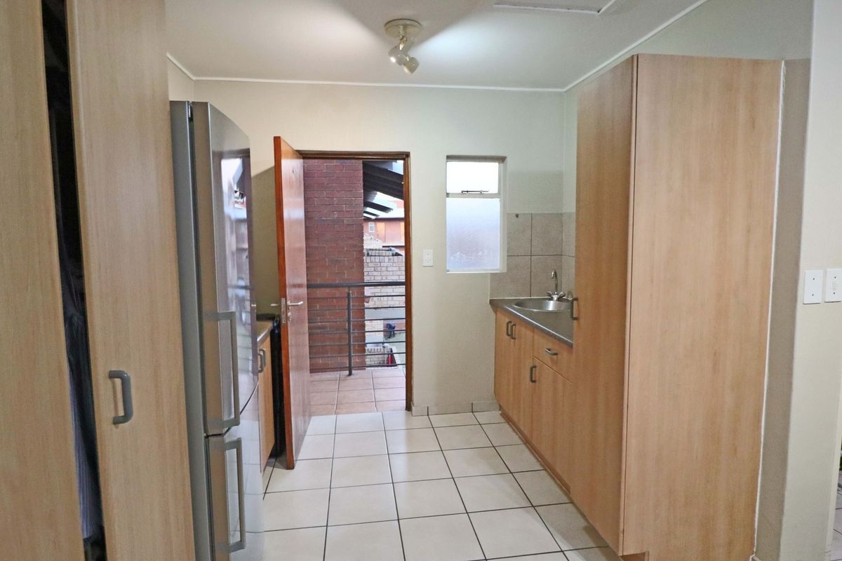 A functional kitchen featuring light wood cabinetry, tiled flooring, and a stainless steel sink, with direct access to an outdoor balcony area.