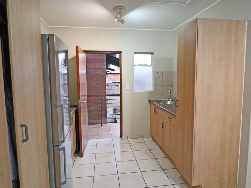 A functional kitchen featuring light wood cabinetry, tiled flooring, and a stainless steel sink, with direct access to an outdoor balcony area.