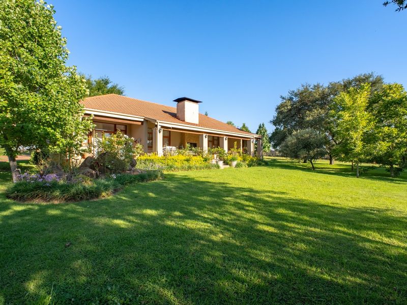 A well-maintained rear elevation of the house featuring a spacious covered patio, a prominent chimney, and an expansive, lush green garden.