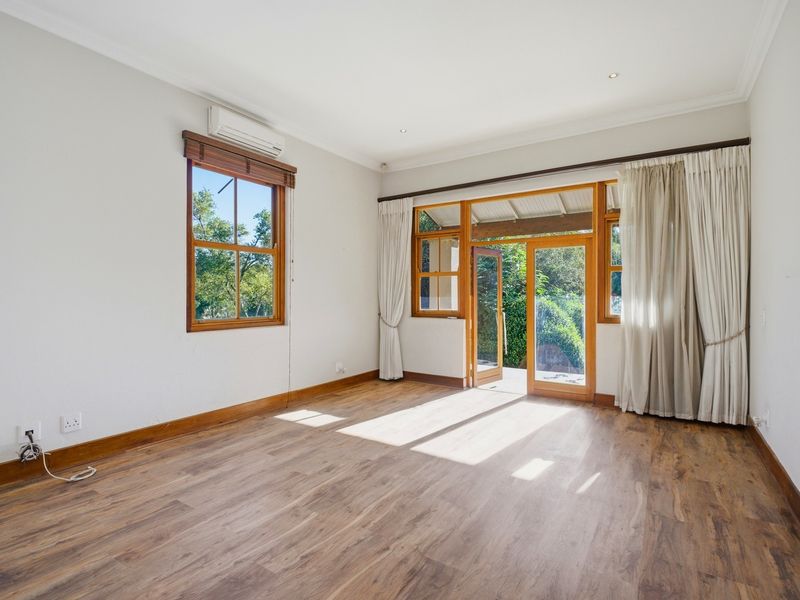 Bright and spacious living area featuring timber-framed windows and doors, laminate flooring, and a split-system air conditioner, with direct access to the outdoor space.