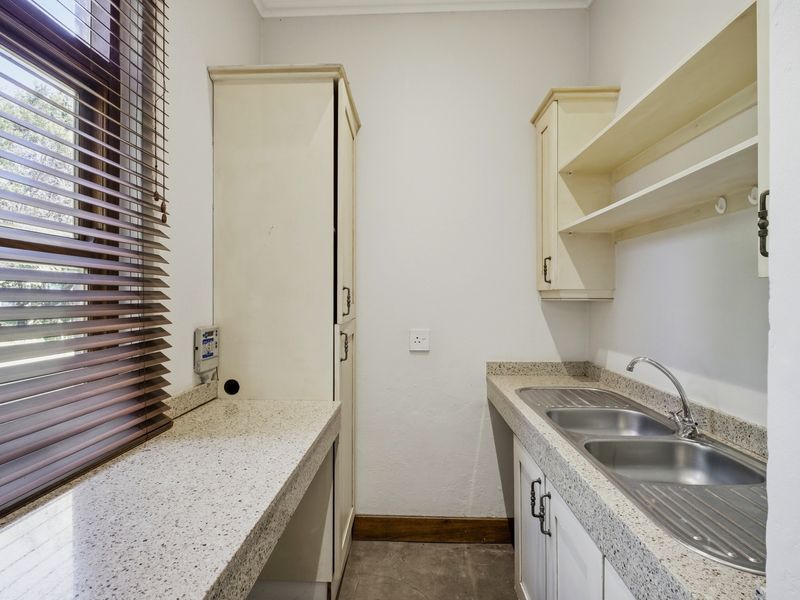 A functional laundry room featuring granite countertops, a double stainless steel sink, built-in cabinetry, and open shelving for storage.