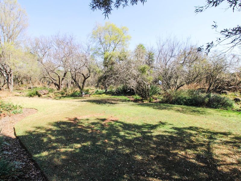 A spacious, established garden featuring a well-maintained lawn area surrounded by mature trees and natural landscaping.