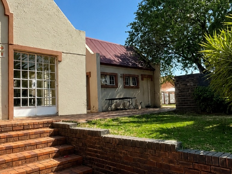 Rear exterior view of the property featuring a brick staircase, retaining wall, and a metal-framed glass entrance door.