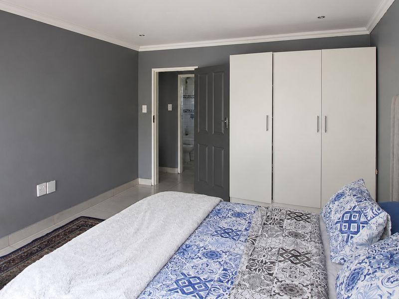 A well-maintained bedroom featuring built-in cupboards, tiled flooring, and recessed downlighting, with direct access to an en-suite bathroom.