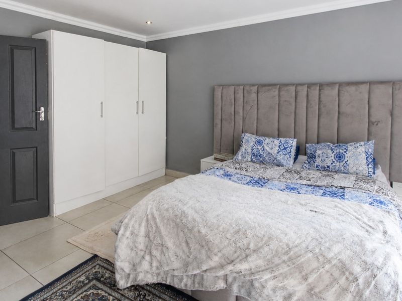 A well-maintained bedroom featuring neutral grey walls, tiled flooring, built-in white cupboards, and a modern upholstered headboard.