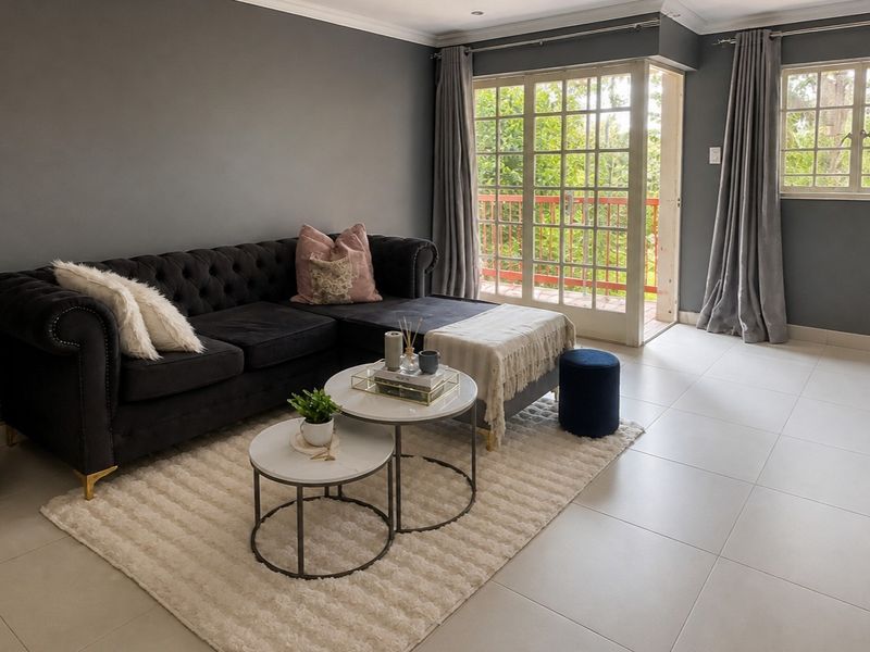 A well-maintained living room featuring neutral tiled flooring, coved cornicing, and direct access to an outdoor balcony through classic French doors.